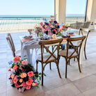 Dining table set with floral arrangements on a balcony with ocean view