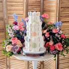Decorative cake with colorful polka dot design surrounded by flowers on a wooden background