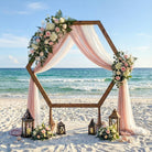 Hexagonal wedding arch on a beach with floral decorations and lanterns.