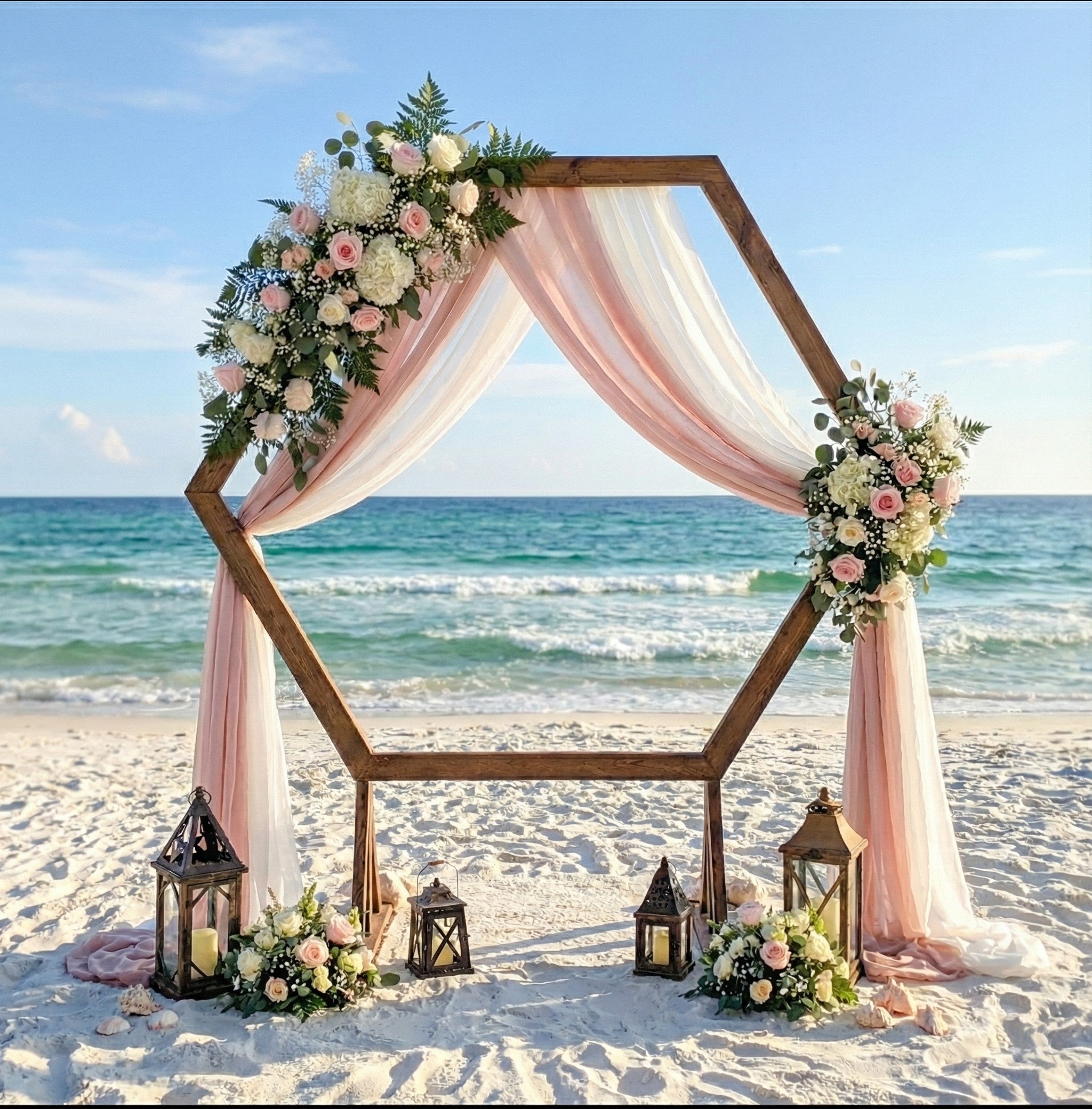 Hexagonal wedding arch on a beach with floral decorations and lanterns.
