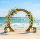 Decorative circle wedding arch with flowers and lanterns on a beach with ocean view