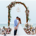 Decorative arch with flowers and a chandelier on a beach, with a couple standing underneath.