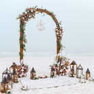 Decorative arch with flowers and lanterns on a sandy beach.